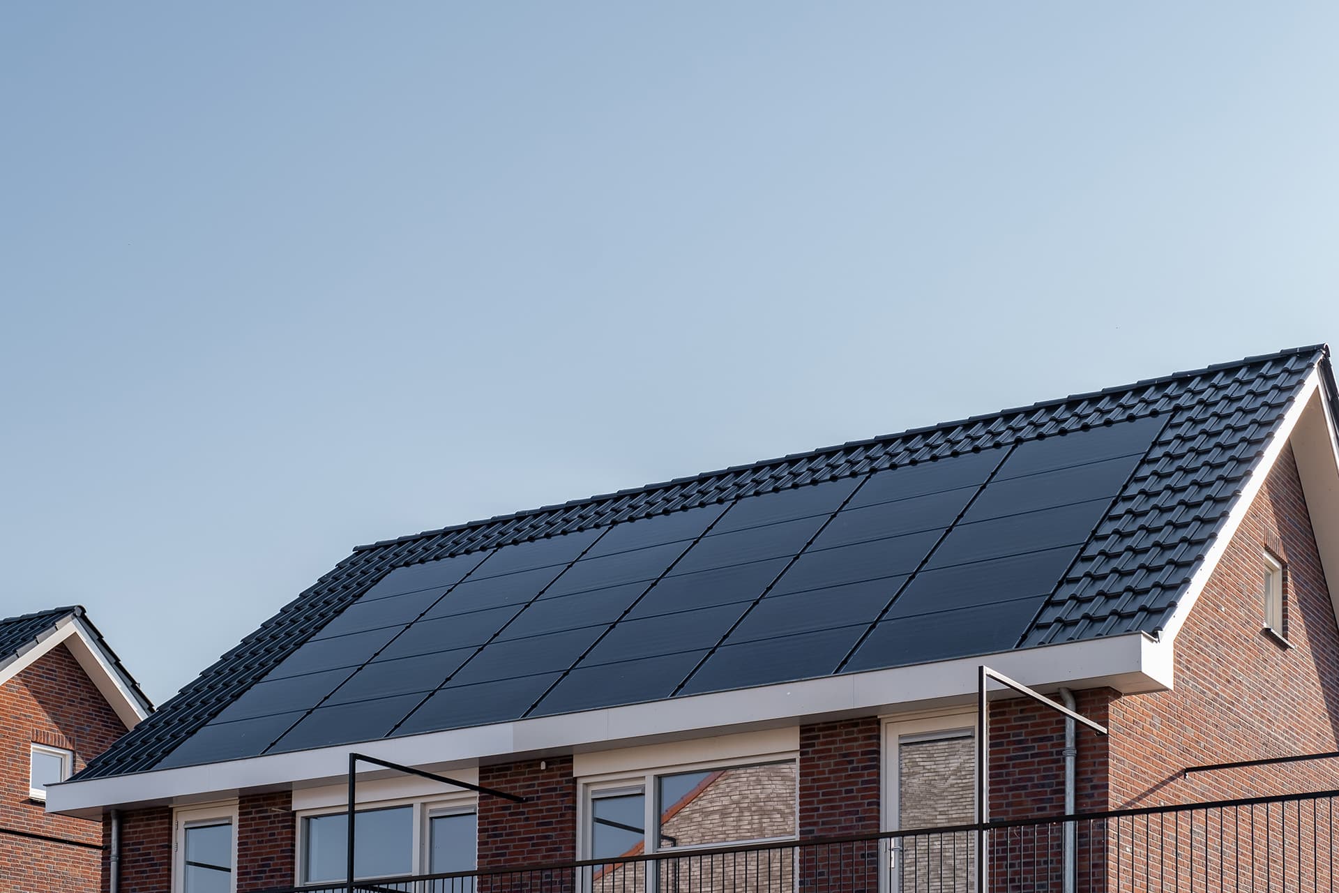 sleek black solar panel system on roof of brown house with a clear blue sky background
